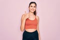 Young beautiful fitness woman wearing sport excersie clothes over pink background doing happy thumbs up gesture with hand Royalty Free Stock Photo