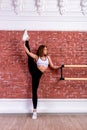 Young beautiful flexible girl in white crop top and black leggings is posing in dance studio. Stretching and body ballet theme.