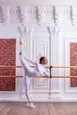 Young beautiful flexible girl in white jumpsuit is posing in a dance studio. Stretching and body ballet theme. Modern dance trend