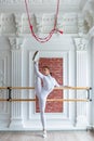 Young beautiful flexible girl in white jumpsuit is posing in a dance studio. Stretching and body ballet theme. Modern dance trend