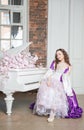 Young beautiful flirtatious woman in fantasy rococo style medieval dress sitting near piano with pink flowers