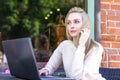 Young beautiful freelancer Caucasian girl is sitting in a street bar and working remotely on her laptop Royalty Free Stock Photo