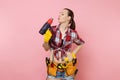 Young beautiful fun handyman woman in plaid shirt, denim shorts, kit tools belt full of variety instruments holding Royalty Free Stock Photo