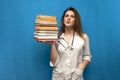 Young beautiful funny girl the nurse holds many books on a blue background and is surprised, the student is studying in a medical Royalty Free Stock Photo