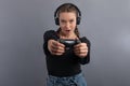 Young beautiful gamer woman playing video game and using joystick and headphones on grey background. Emotional face. Gambler