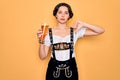 Young beautiful german woman with blue eyes wearing octoberfest dress drinking glass of beer with angry face, negative sign Royalty Free Stock Photo