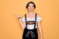 Young beautiful german woman with blue eyes wearing traditional octoberfest dress smiling cheerful presenting and pointing with