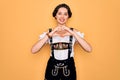 Young beautiful german woman with blue eyes wearing traditional octoberfest dress smiling in love doing heart symbol shape with