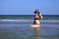 Young beautiful girl in a bathing suit and a striped hat is sitting on the seashore with her hand on the brim hat