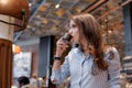 Young beautiful girl in a beautiful modern cafe drinks delicious coffee. Girl in a fashionable blue shirt Royalty Free Stock Photo