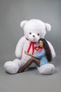 Young beautiful girl with big teddy bear soft toy happy smiling and playing on grey background Royalty Free Stock Photo