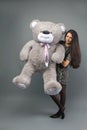 Young beautiful girl with big teddy bear soft toy happy smiling and playing on grey background Royalty Free Stock Photo