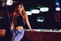 Young beautiful girl in a billiard club, with cue stick posing