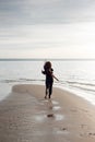 Young beautiful girl in black clothes walking on the beach. She walks along shore. A walk at sunset. Nobody around Royalty Free Stock Photo