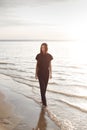Young beautiful girl in black clothes walking on the beach. She walks along shore. A walk at sunset. Nobody around. Laugh, smile a Royalty Free Stock Photo
