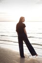 Young beautiful girl in black clothes walking on the beach. She walks along shore. A walk at sunset. Nobody around. Laugh, smile a Royalty Free Stock Photo