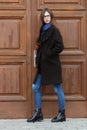 Young beautiful girl in a black coat and blue scarf having fun. Elegant brunette girl with gorgeous extra long hair against wooden Royalty Free Stock Photo