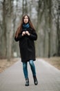 Young beautiful girl in a black coat and blue scarf for a walk in the autumn / spring park. An elegant brunette girl with gorgeous