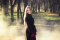 Young beautiful girl in a black coat red gloves exploring spring forest smoke park.