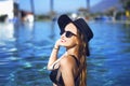 Young beautiful girl in black fashion hat smile, velvet skin, red lips, black swimsuit posing in the pool in blue water Royalty Free Stock Photo