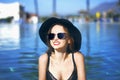 Young beautiful girl in black fashion hat smile, velvet skin, red lips, black swimsuit posing in the pool in blue water Royalty Free Stock Photo
