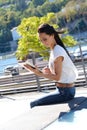 Young beautiful girl black hair in the wind using tablet outside in the summer on the street with green river background