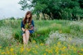 Young beautiful girl in a blue dress and jean jacket with a bouquet of wildflowers sits on the green grass.
