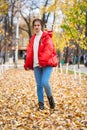 Young beautiful girl in blue jeans and red down jacket posing in autumn leaves in a park Royalty Free Stock Photo