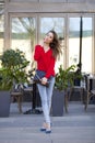 Young beautiful girl in blue jeans and red shirt on the background of summer street Royalty Free Stock Photo