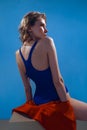 A young beautiful girl in a blue swimsuit sits with her back. Evening light and blue background. Royalty Free Stock Photo