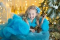 Young beautiful girl in blue white elegant evening dress sitting on floor near christmas tree and presents on a new year Royalty Free Stock Photo