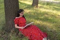 A young beautiful girl with a book is leaning against the trunk of a large tree and is resting in nature in the park. The brunette Royalty Free Stock Photo
