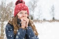 Young beautiful girl breathes on her hands so that it is warmer, under soft fluffy snow on a winter day