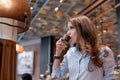 Young beautiful girl in a cafe drinks aromatic delicious coffee. Girl in a fashionable blue shirt Royalty Free Stock Photo