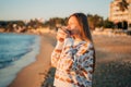 Young beautiful girl in cozy sweater drinking coffee on a winter seaside shore while taking sunbathe in a mild sunset Royalty Free Stock Photo