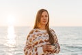 Young beautiful girl in cozy sweater holding coffee cup while enjoying winter sun on seaside shore during mild sunset Royalty Free Stock Photo