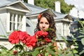 Beautiful girl with curls next to red roses in the garden