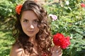 Beautiful girl with curls next to red roses in the garden