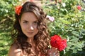 Beautiful girl with curls next to red roses in the garden