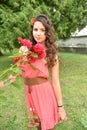 Beautiful girl with curls next to red roses in the garden