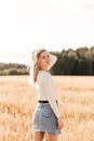 A young beautiful girl in a denim skirt walks through a wheat field on a sunny day Royalty Free Stock Photo