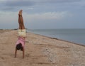 A young beautiful girl does a handstand on the beach. A teenage girl stands on her hands on the sandy beach near the water`s edge