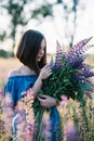 Young beautiful girl in a dress stands in a field of lupins. Girl holds a large bouquet of purple lupins in a flowering field. Royalty Free Stock Photo