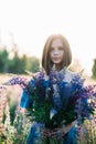 Young beautiful girl in a dress stands in a field of lupins. Girl holds a large bouquet of purple lupins in a flowering field. Royalty Free Stock Photo