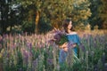 Young beautiful girl in a dress stands in a field of lupins. Girl holds a large bouquet of purple lupins in a flowering field. Royalty Free Stock Photo