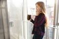 Young beautiful girl drinking coffee and talking on the phone, a woman in an office building Royalty Free Stock Photo