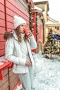 A young and beautiful girl is drinking tea or coffee from a red mug. In winter city. Against the background of red and Royalty Free Stock Photo