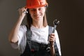 Young beautiful girl engineer in a gray uniform and protective helmet smiles with tools, wrenches in her hands. Equality between Royalty Free Stock Photo