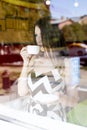 Young beautiful girl in glass showcase a cafe, sunny day, holding mug of tea Royalty Free Stock Photo