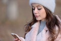 Young beautiful girl in a gray fluffy hat and a pink coat look at the smartphone Royalty Free Stock Photo